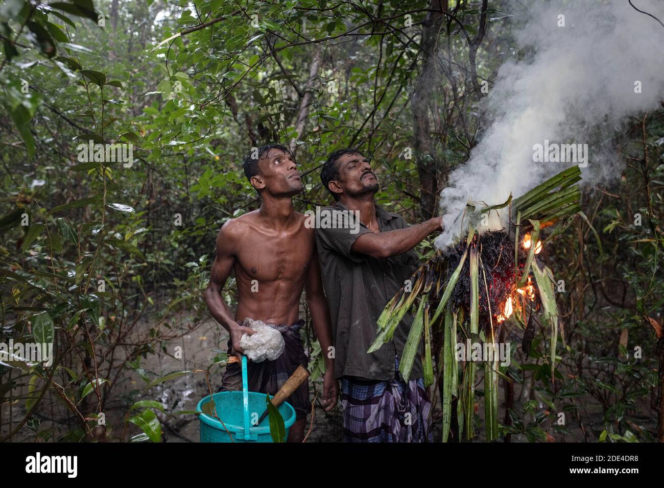 Zwei Honigsammler nach dem Anzünden von feuchten Stauden und Blättern mit Brandbeschleuniger, um Rauch zu erzeugen, Mongla, Sundarbans, Bangladesch Stockfoto
