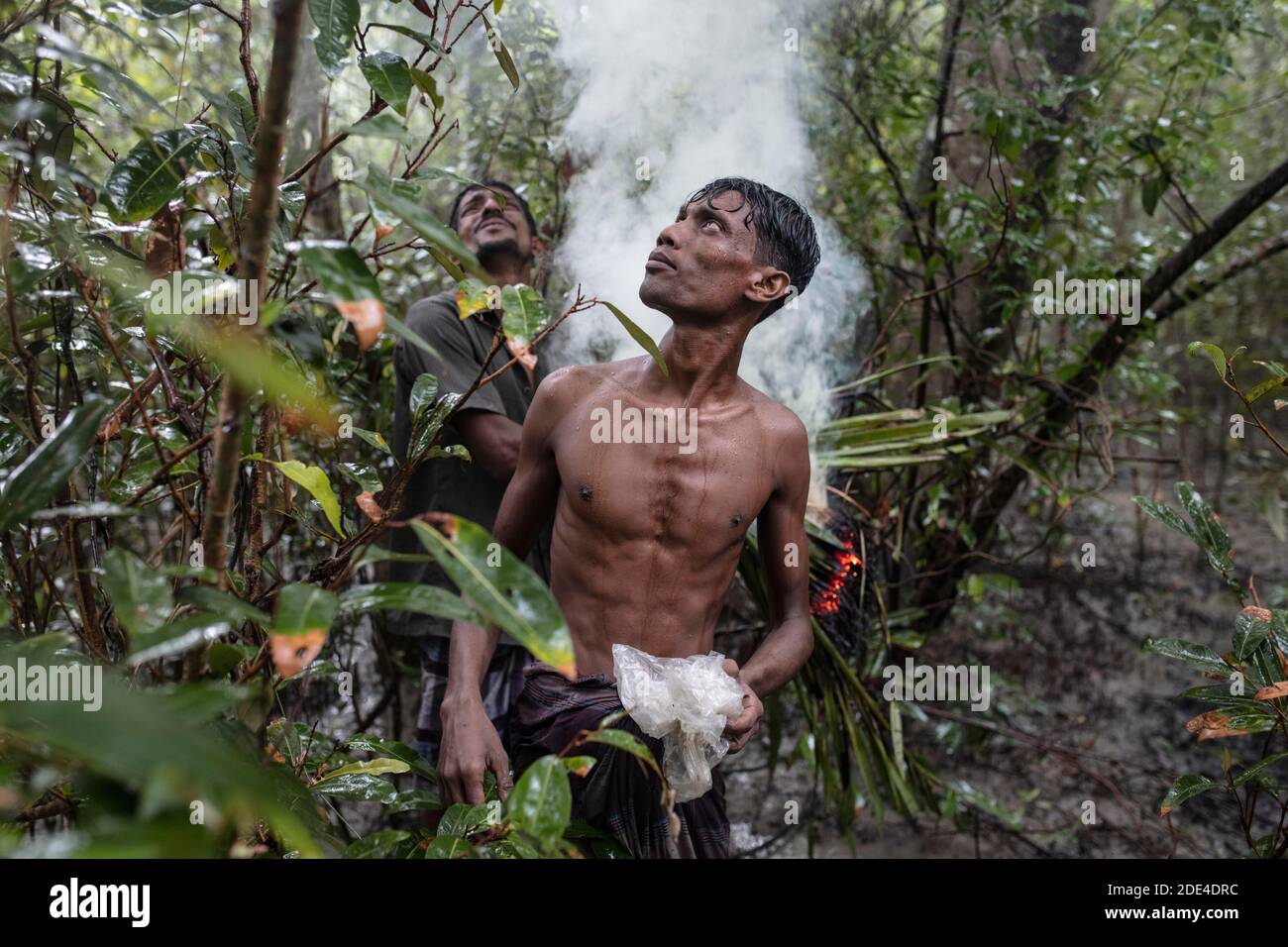 Zwei Honigsammler nach dem Anzünden von feuchten Stauden und Blättern mit Brandbeschleuniger, um Rauch zu erzeugen, Mongla, Sundarbans, Bangladesch Stockfoto