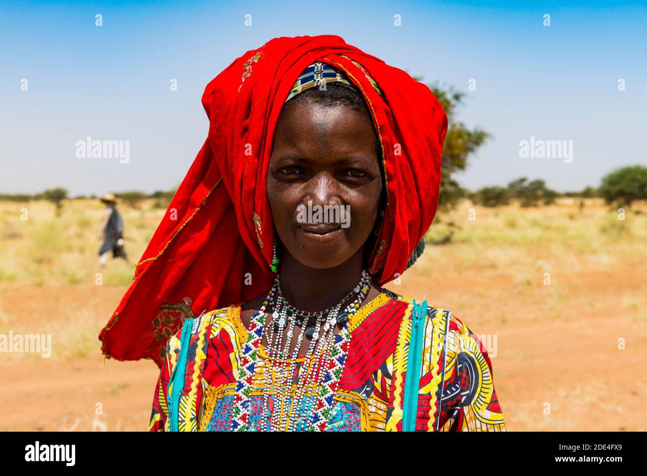 Bunt gekleidete Frau reist mit einer Karawane von Peul-Nomaden Und ihre Tiere in der Sahelzone von Niger Stockfoto