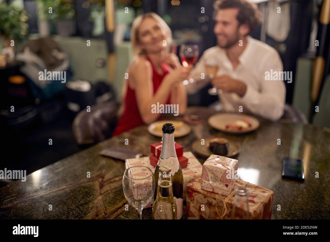 Junge kaukasische Paar beim Abendessen in einem Restaurant, feiert Neujahr. Konzentrieren Sie sich auf Geschenke, Getränke und Glas Stockfoto