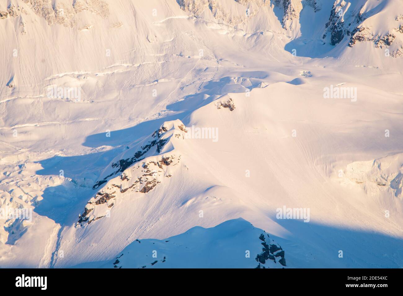 Weißer Schnee auf den hohen Bergen erhellte sich bei Sonnenaufgang und warf lange weiche Schatten Stockfoto