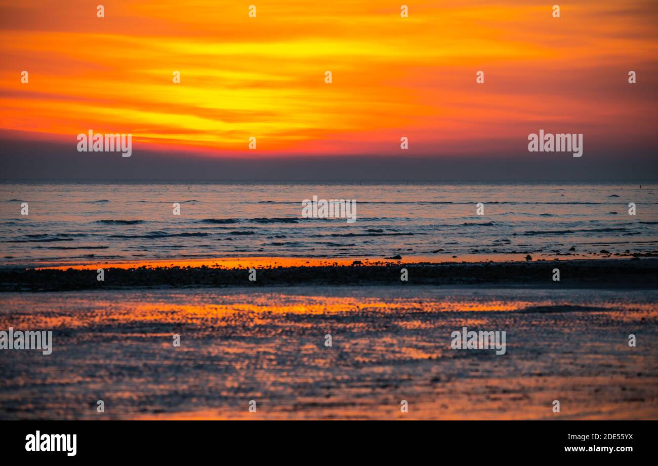 Orangerot Himmel kurz nach Sonnenuntergang an der Küste, zeigt Sonne im Meer in Großbritannien reflektiert. Stockfoto
