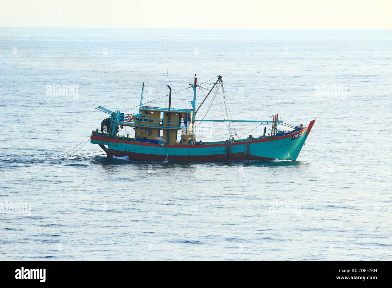 Traditionelles myanmarisches/burmesisches Fischerboot, das bei ruhigem Wetter mit 3 Personen an Bord in der Andamanensee geschleppt wird Stockfoto