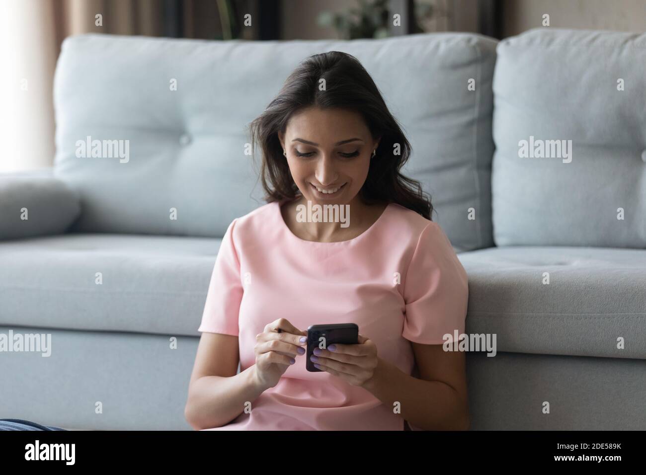 Lächelnde Millennial multiracial Frau mit Smartphones, sitzen auf dem Boden. Stockfoto