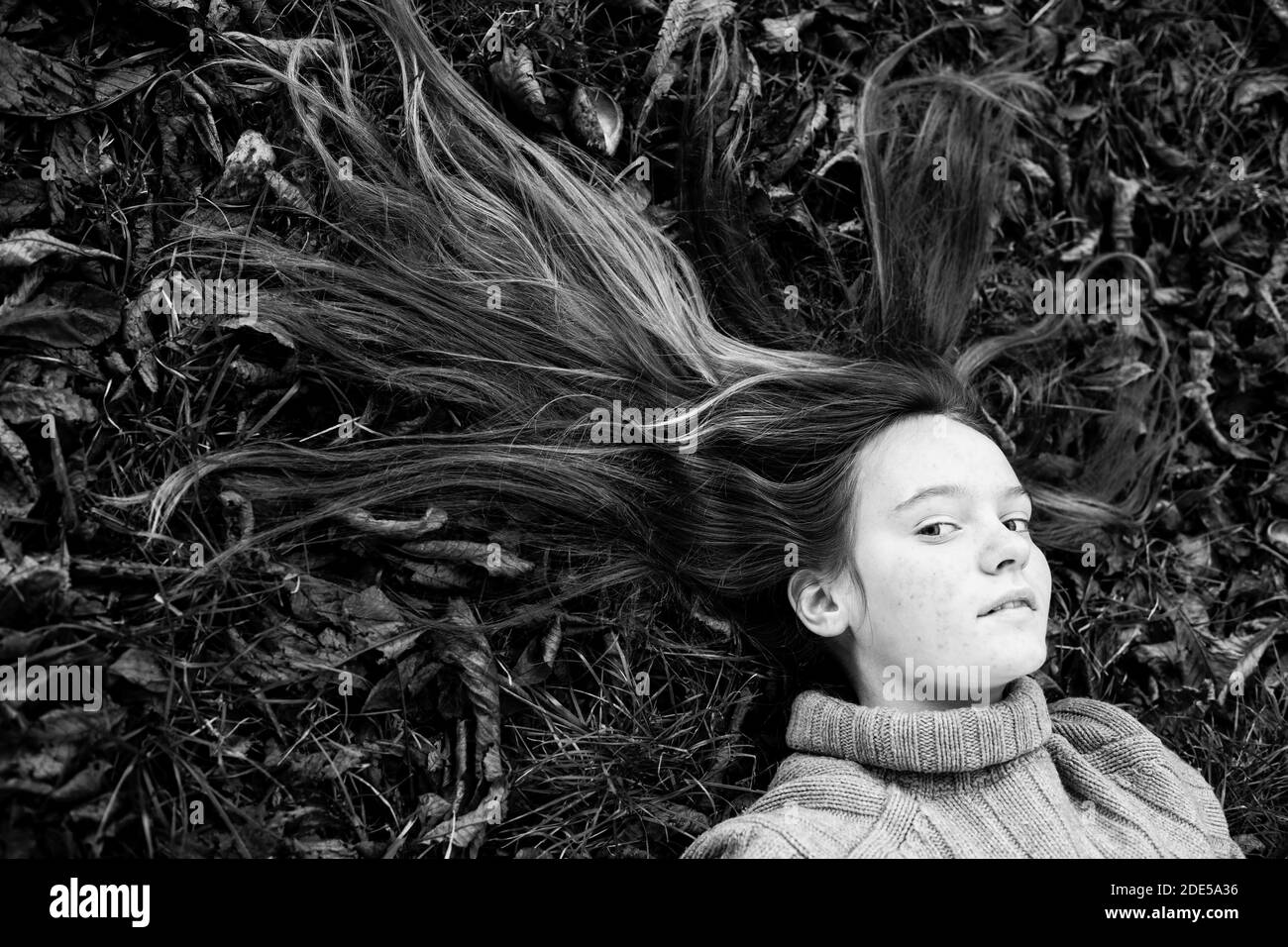 Junges Mädchen liegt auf Herbstboden mit langen Haaren auf dem Gras verstreut. Schwarzweiß-Foto. Stockfoto