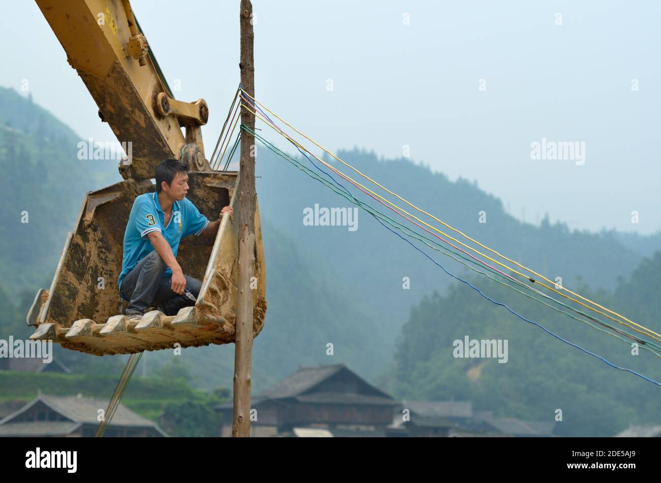 ZHAOXING DONG, CHINA - Juni 21, 2012: chinesischer Arbeiter zur Festsetzung im freien Strom Kabel pylon. Er sitzt die Schaufel des Baggers. Miao Minderheit Stockfoto