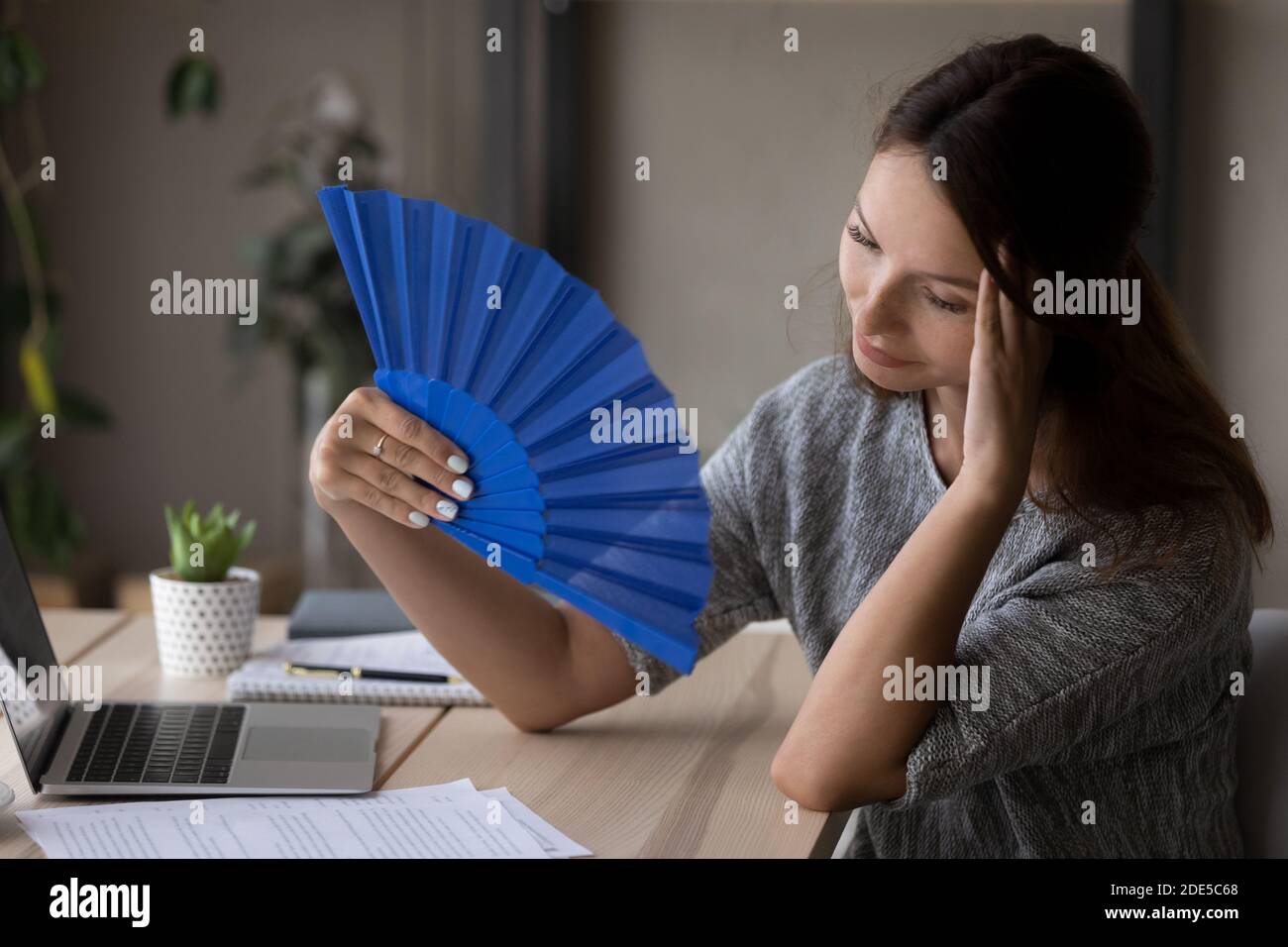 Unglücklich ängstlich Frau weht frische Luft mit Papierventilator. Stockfoto