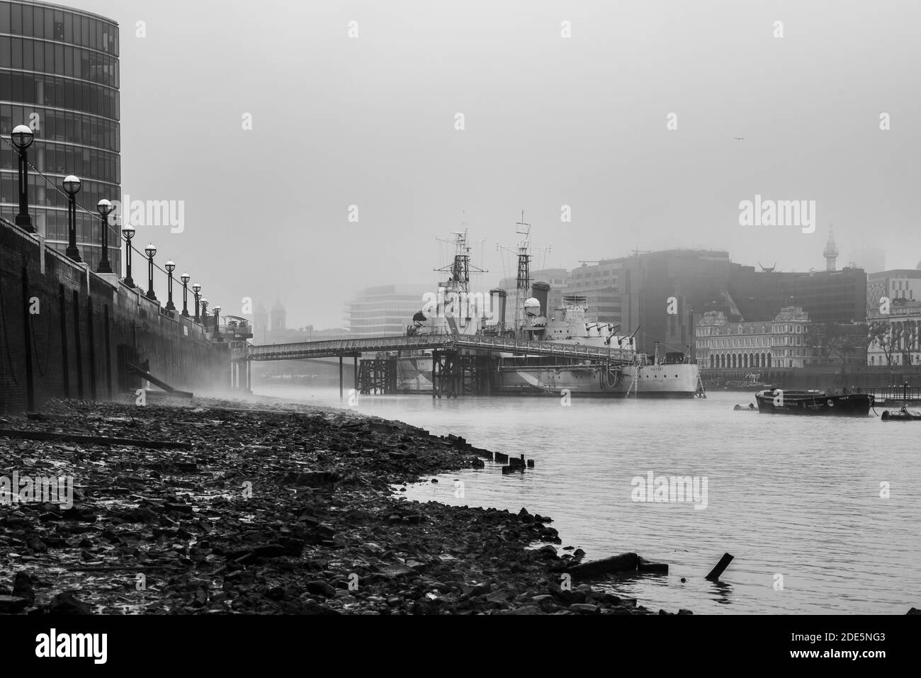 Schwarz-weiß HMS Belfast Royal Navy Schiff in der Themse bei Ebbe von einem Themse Strand in London in nebligen nebligen Wetter angedockt, erschossen in Coronavirus Covid-19 Lockdown in England, Europa Stockfoto