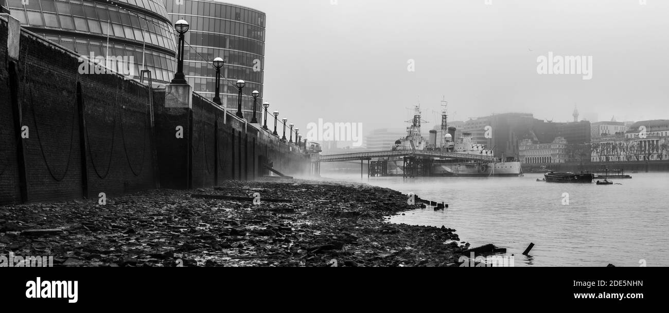 Schwarz-weiß HMS Belfast Royal Navy Schiff in der Themse bei Ebbe von einem Themse Strand in London in nebligen nebligen Wetter angedockt, erschossen in Coronavirus Covid-19 Lockdown in England, Europa Stockfoto