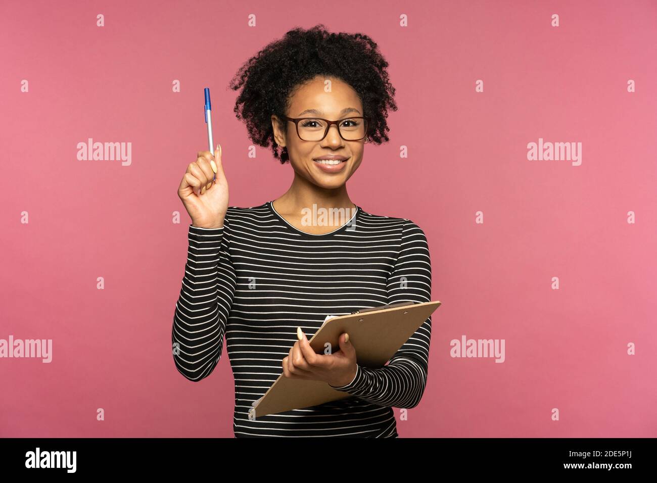 Junge glückliche afro-amerikanische Lehrerin Frau isoliert auf rosa Studio Wand. Student Mädchen tragen Brille halten Ordner und Stift, lächelnd, Blick auf die Kamera. Ed Stockfoto