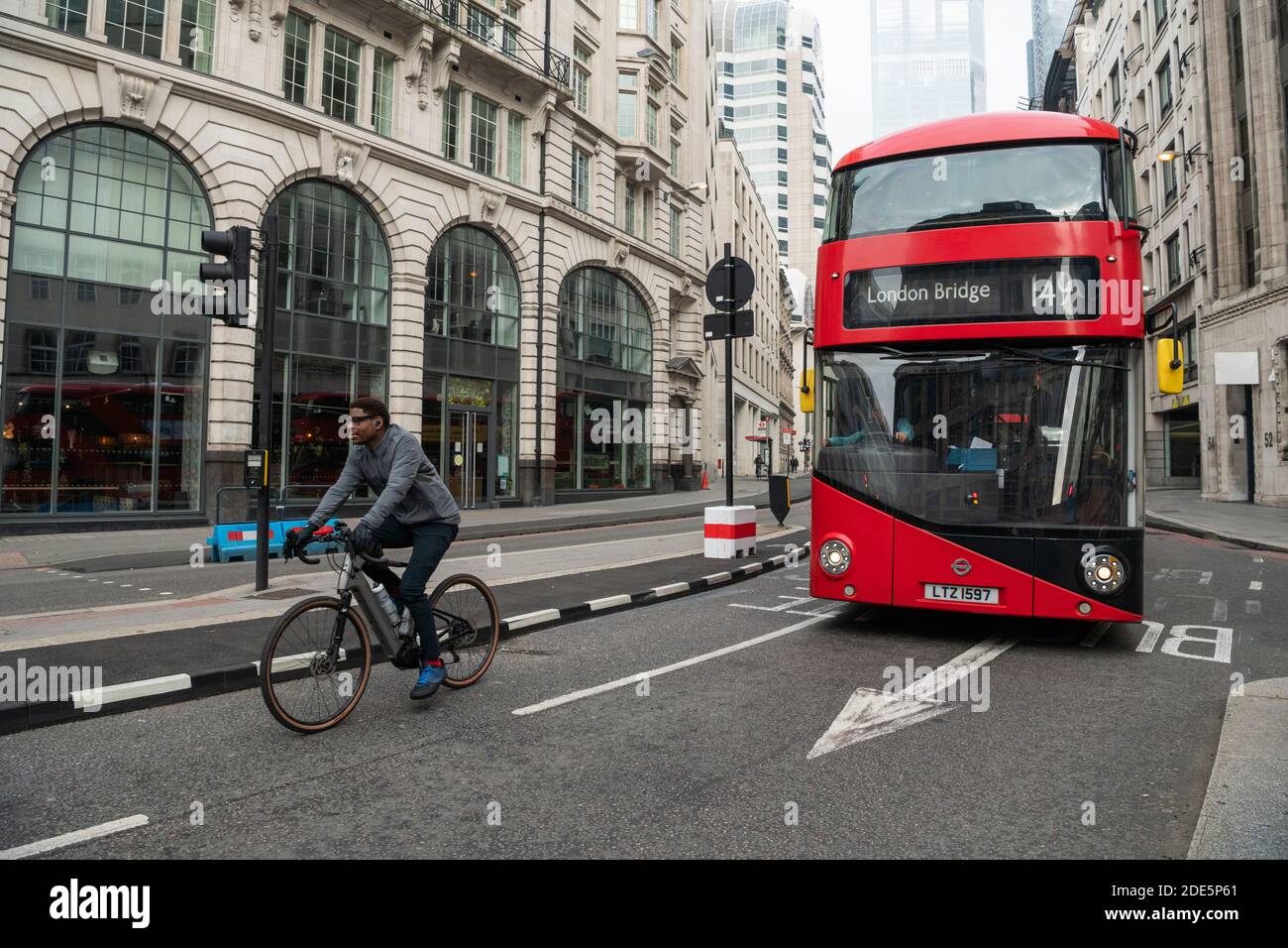 Ruhige Straßen und Straßen in der City im Zentrum von London mit nur einem roten London Bus für öffentliche Verkehrsmittel, und ein Radfahrer auf einem Fahrrad während Coronavirus Covid-19 Sperre in England, Großbritannien, Europa genommen Stockfoto
