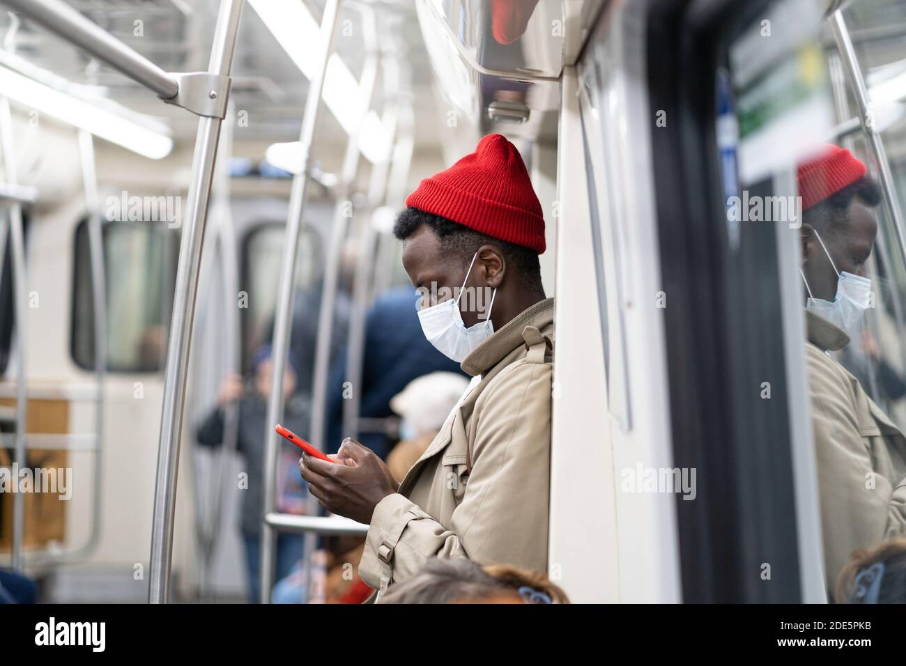 Afro-amerikanische Passagiermann stehen in U-Bahn-Zug, tragen Gesicht medizinische Maske, um sich vor Grippe-Virus, covid-19, Coronavirus, mit mobilen Phon zu schützen Stockfoto