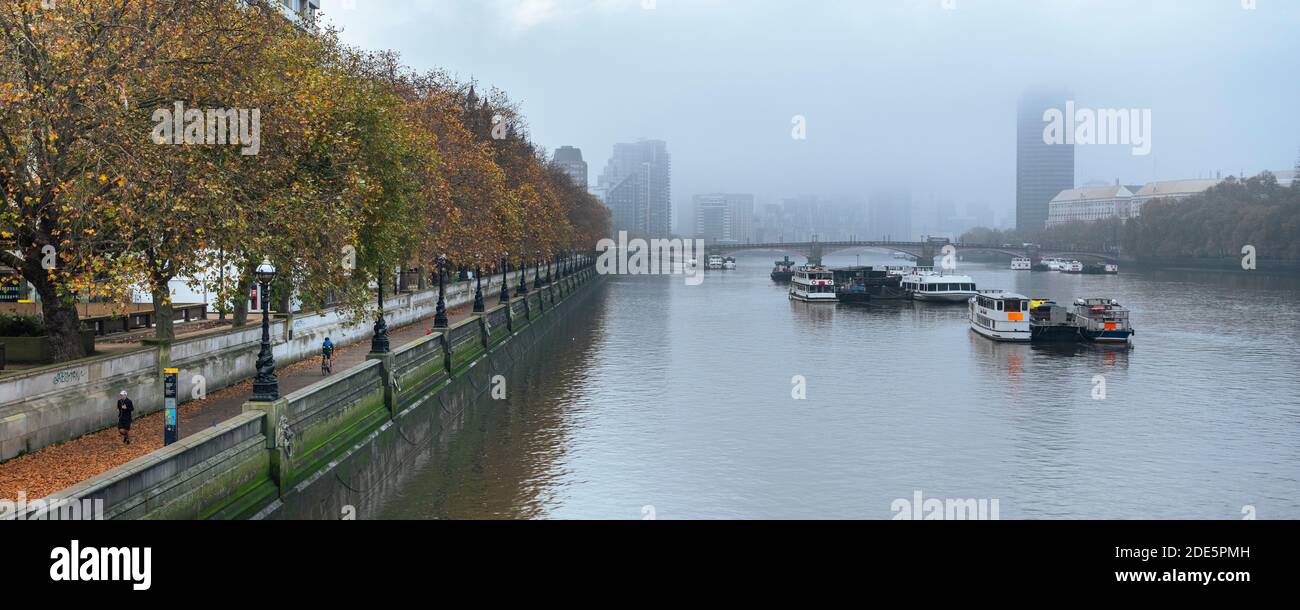London in Coronavirus Covid-19 Lockdown mit Menschen Joggen und Radfahren entlang der Themse auf South Bank mit Herbstbäumen bei atmosphärisch nebligen Wetter in England, Großbritannien zur Rush Hour Stockfoto