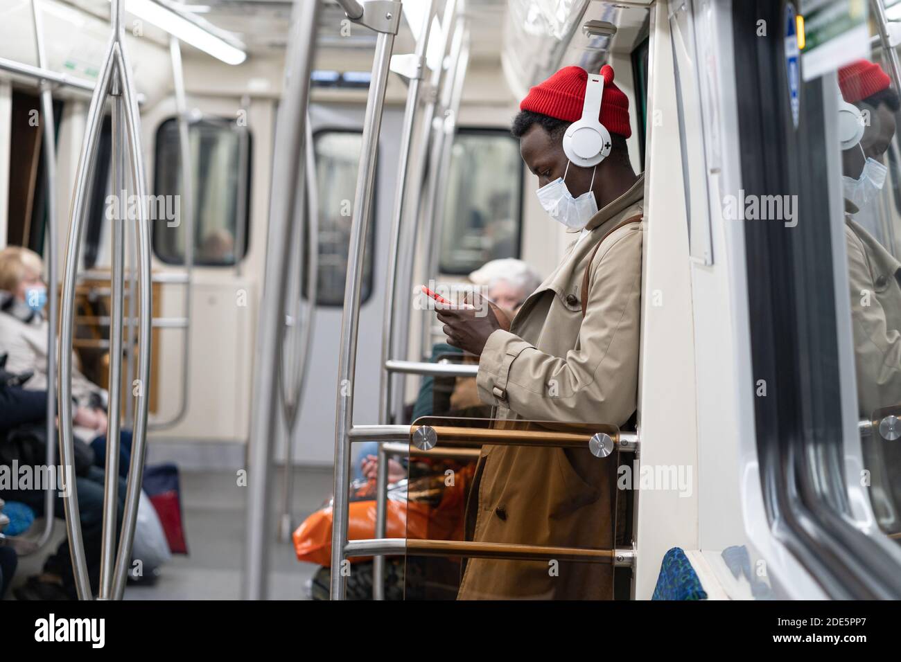 Afro-amerikanische Passagiermann stehen in U-Bahn-Zug, tragen Gesicht medizinische Maske, um sich vor Grippe-Virus, covid-19, Coronavirus, mit mobilen Phon zu schützen Stockfoto