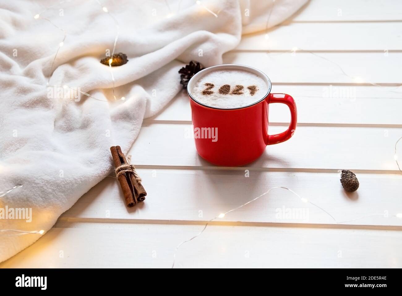 Nummer 2021 auf der schaumigen Cappuccino-Oberfläche serviert in einem roten Becher auf dem gemütlichen karierten und weihnachtlichen Hintergrund. Food Art kreatives Konzept für Neues Stockfoto