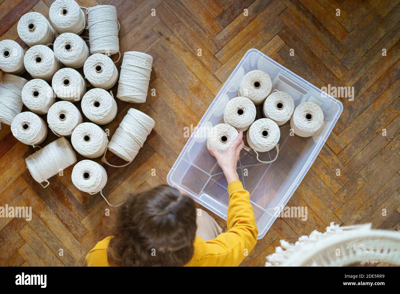 Draufsicht auf Frau Freiberuflerin, die weiße Macrame Baumwollseile in Skeins hält, legt Arbeitsmaterial in eine Plastikbox. Häkeln, Weben Handwerk Stockfoto
