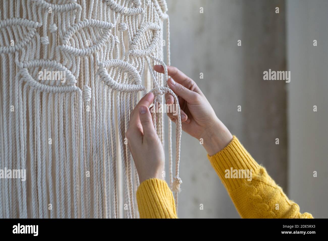Nahaufnahme der freiberuflichen Frau arbeiten an halb fertig macrame Stück, webt Lampenschirm für Kronleuchter. Frauen Hobby. Stockfoto