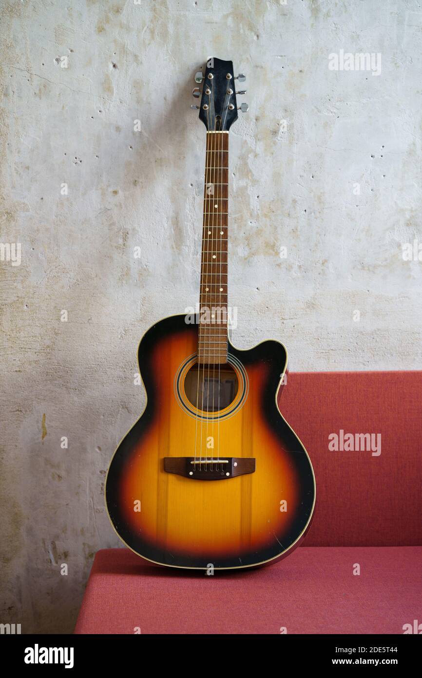 Akustische Vintage schwarz und orange Gitarre auf roter Couch im Loft-Stil Wohnung über Betonwand. Vertikal. Stockfoto