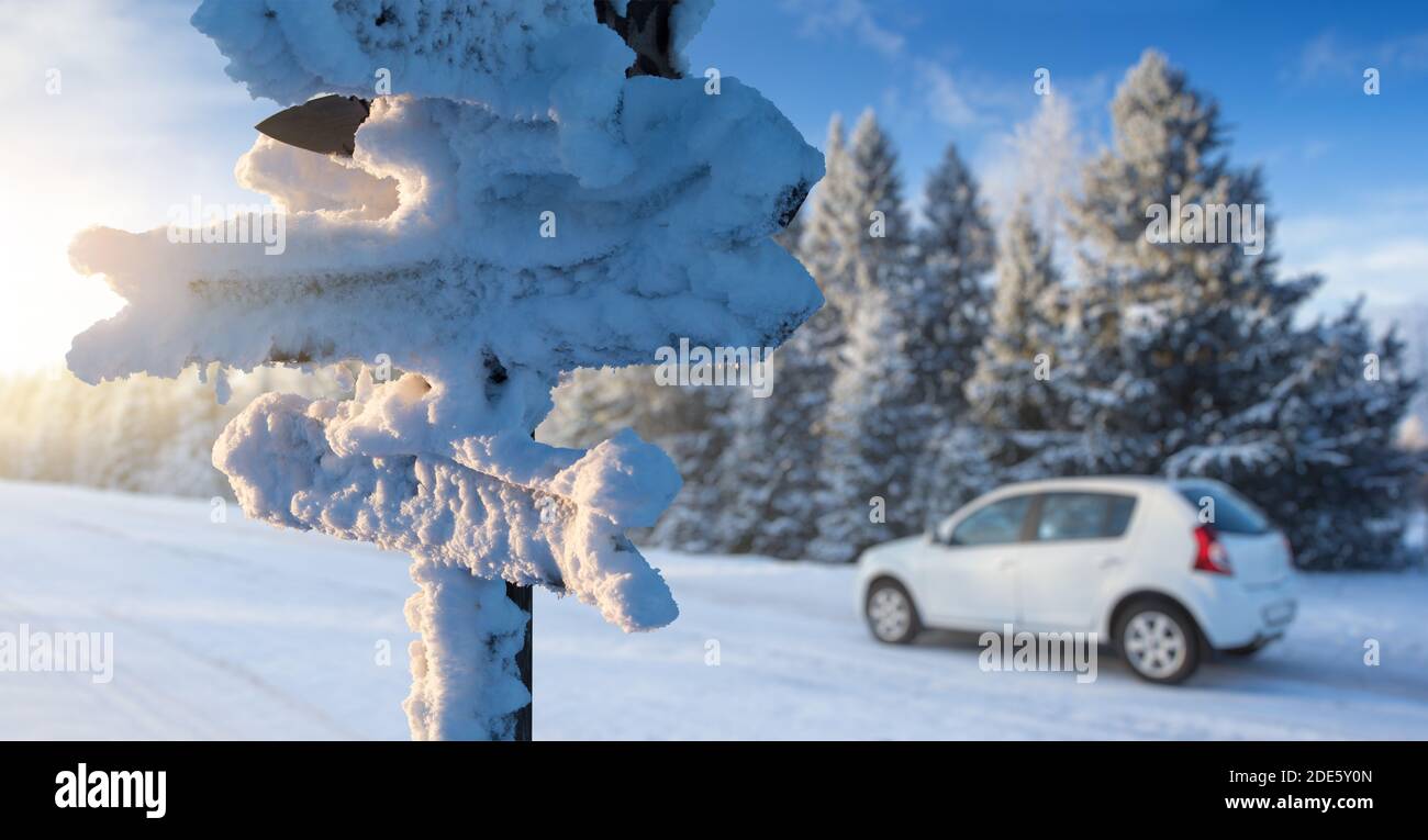 Schneebedecktes Schild mit Holzpfeilen auf dem Hintergrund eines Autos auf einer Straße. Reisen im Winter Stockfoto