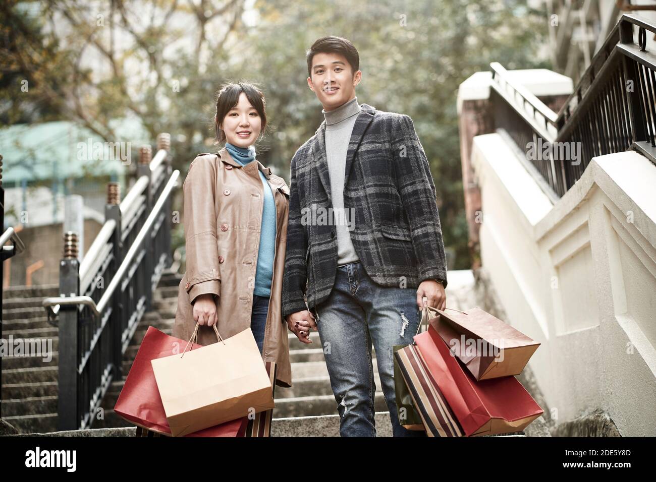 Outdoor-Porträt von glücklich junge asiatische Paar auf Stufen stehen Mit Papier Einkaufstaschen in der Hand Stockfoto