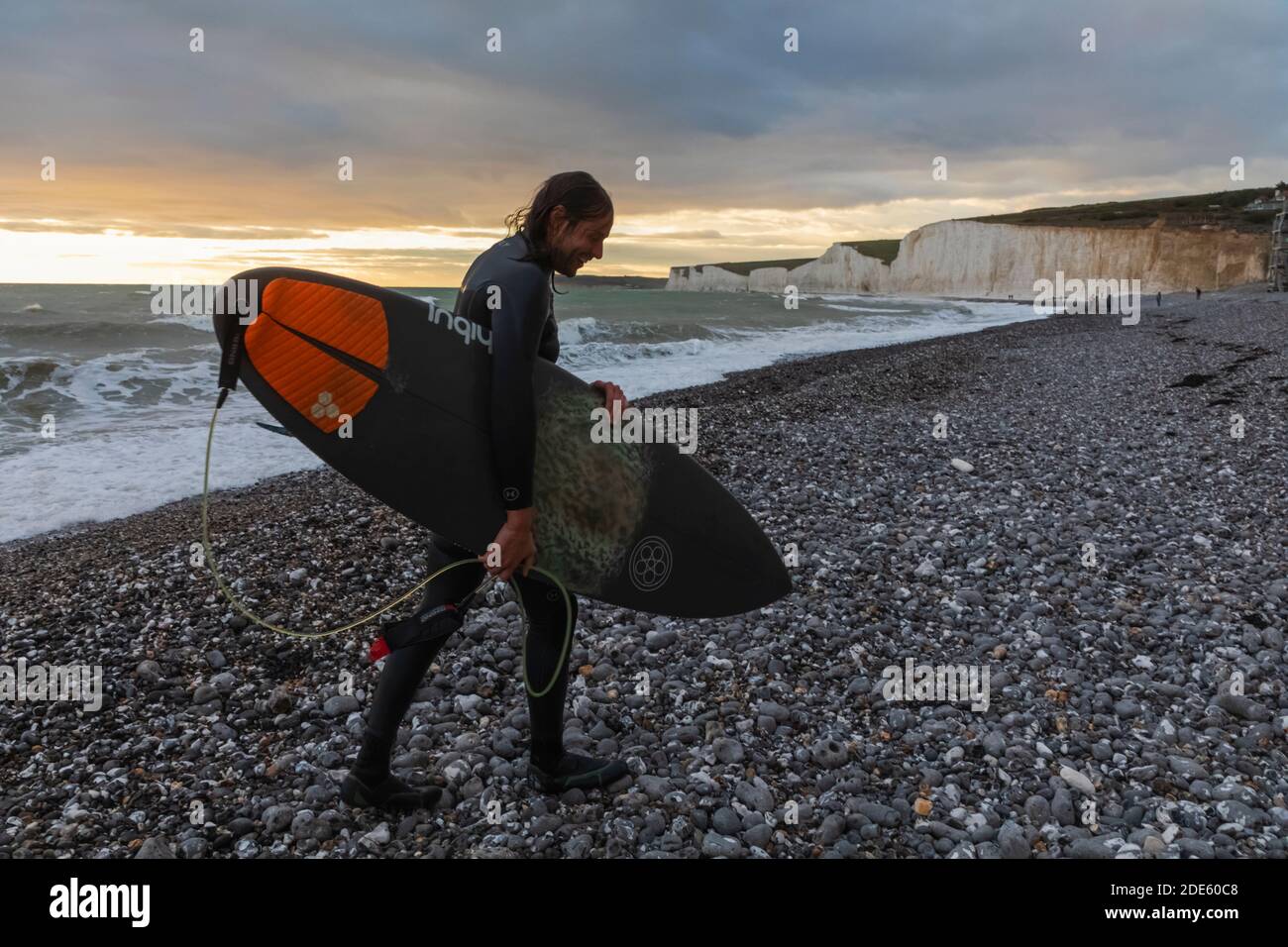 England, East Sussex, Eastbourne, Birling Gap, The Seven Sisters Cliffs and Beach, Male Surfer Walking on Beach mit Surfbrett Stockfoto