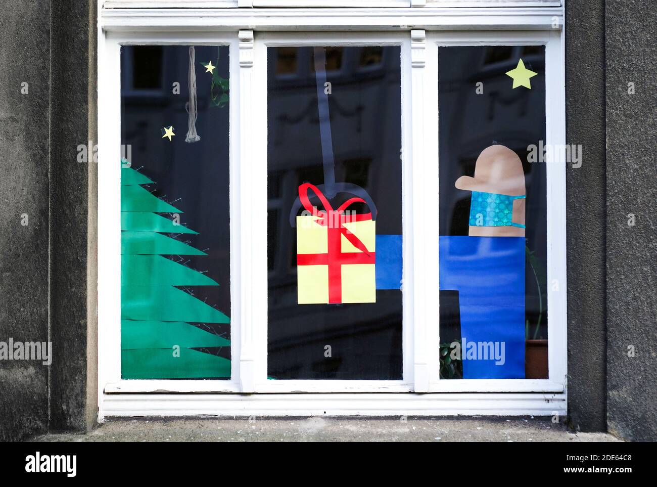 Dortmund, 29. November 2020: Wohnungsfenster zu Weihnachten dekoriert bezieht sich auf den Heiligabend in der Corona-Zeit. Der Mann, der das Geschenk gibt, trägt Mund- und Nasenschutz gegen das Virus. Stockfoto