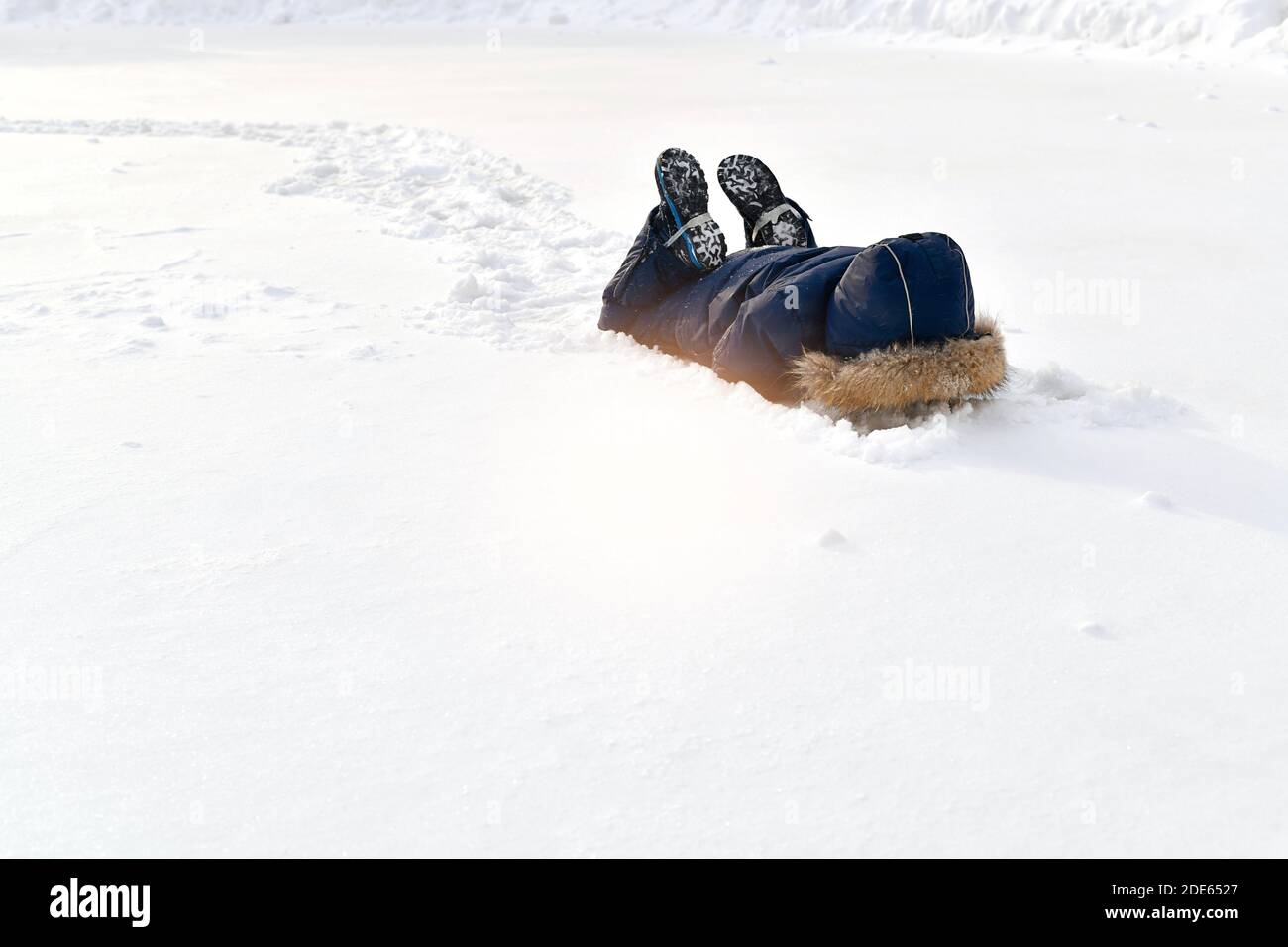 Das Kind spielt im Schnee. Liegen begraben seine Hände und Kopf nach unten, versteckt. An den Füßen stützen die Schuhe die Gurtstifte aus dem Winter-Jumpsuit. Stockfoto