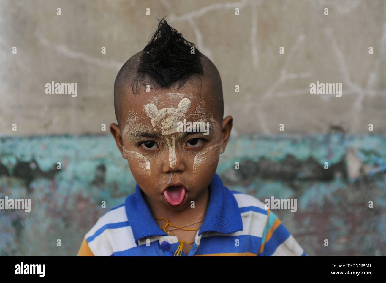 15.01.2014, Yangon, Myanmar, Asien - Porträt eines kleinen Jungen, der seine Zunge heraussticht und Thanaka-Paste auf sein Gesicht aufgetragen hat. Stockfoto