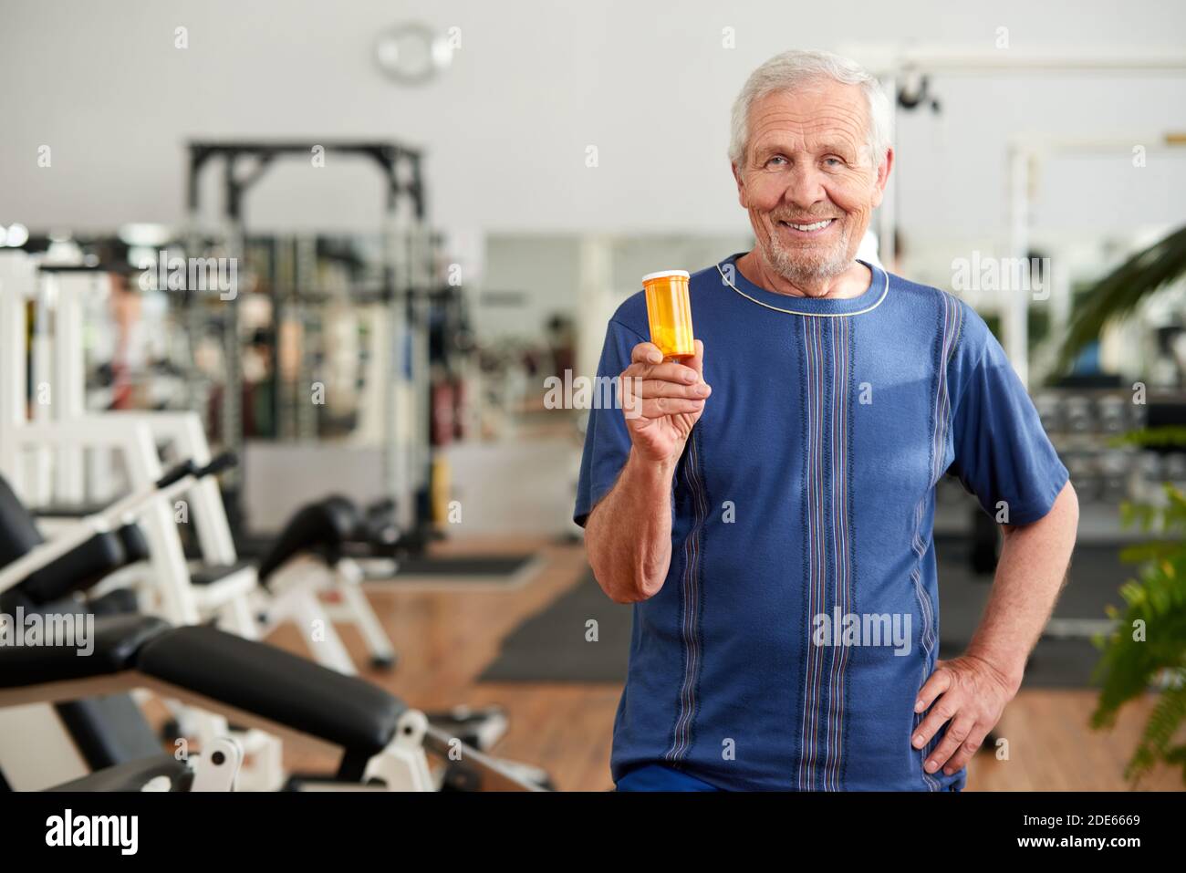 Älterer Mann hält eine Flasche Pillen im Fitnessstudio. Stockfoto