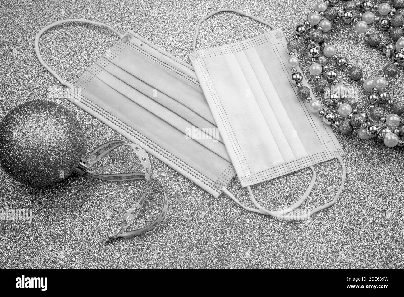 Weihnachtliche graue Zierkugel auf grauem Hintergrund mit zwei chirurgischen Schutzmasken: Für Erwachsene und für Kinder. Neues Jahr in Quarantäne. Flach Lay-Design Stockfoto