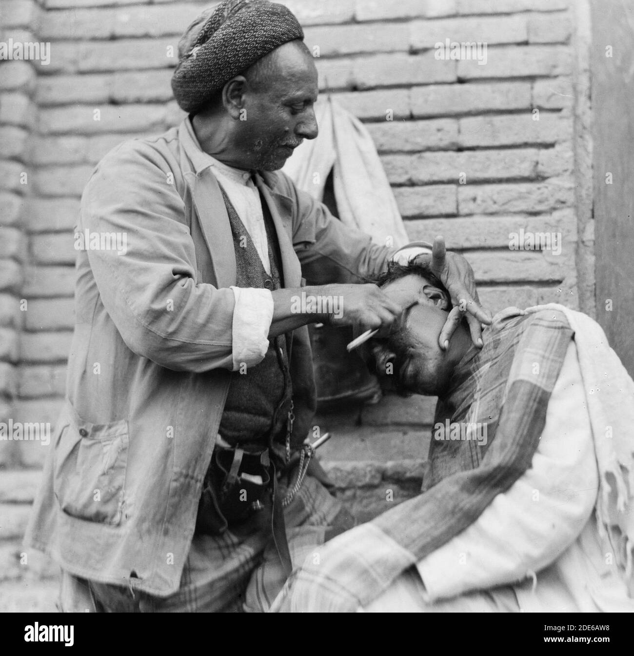 Originalunterschrift: Irak. (Mesopotamien). Bagdad. Ansicht von Straßenszenen und Typen. Straßenbarbier bei der Arbeit - Ort: Irak--Bagdad ca. 1932 Stockfoto