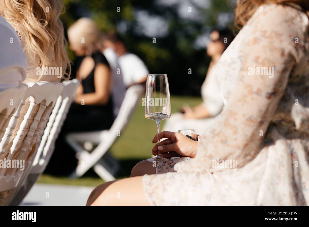 Fceless Frau sitzt auf dem Stuhl mit dem Glas Champagner in den Händen während der Hochzeitszeremonie. Alkoholisches Getränk Stockfoto