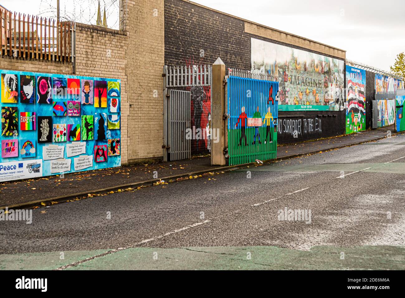 Mehrere Wandgemälde der Internationalen Mauer (auch bekannt als Solidaritätsmauer) säumen die Northumberland Street in Belfast, Nordirland: links ein von Jugendlichen erschaffenes Wandgemälde mit dem Titel „Peace“, das gemeinsam vom EU-PEACE-IV-Programm finanziert wurde und ermutigende Slogans zeigt, und rechts ein Mosaikwandgemälde, das sich auf John Lennons Song „Imagine“ für den Internationalen Tag des Friedens bezieht; zwei bemalte verbarrikadierte Tore unterbrechen die Reihe der Wandgemälde. Stockfoto