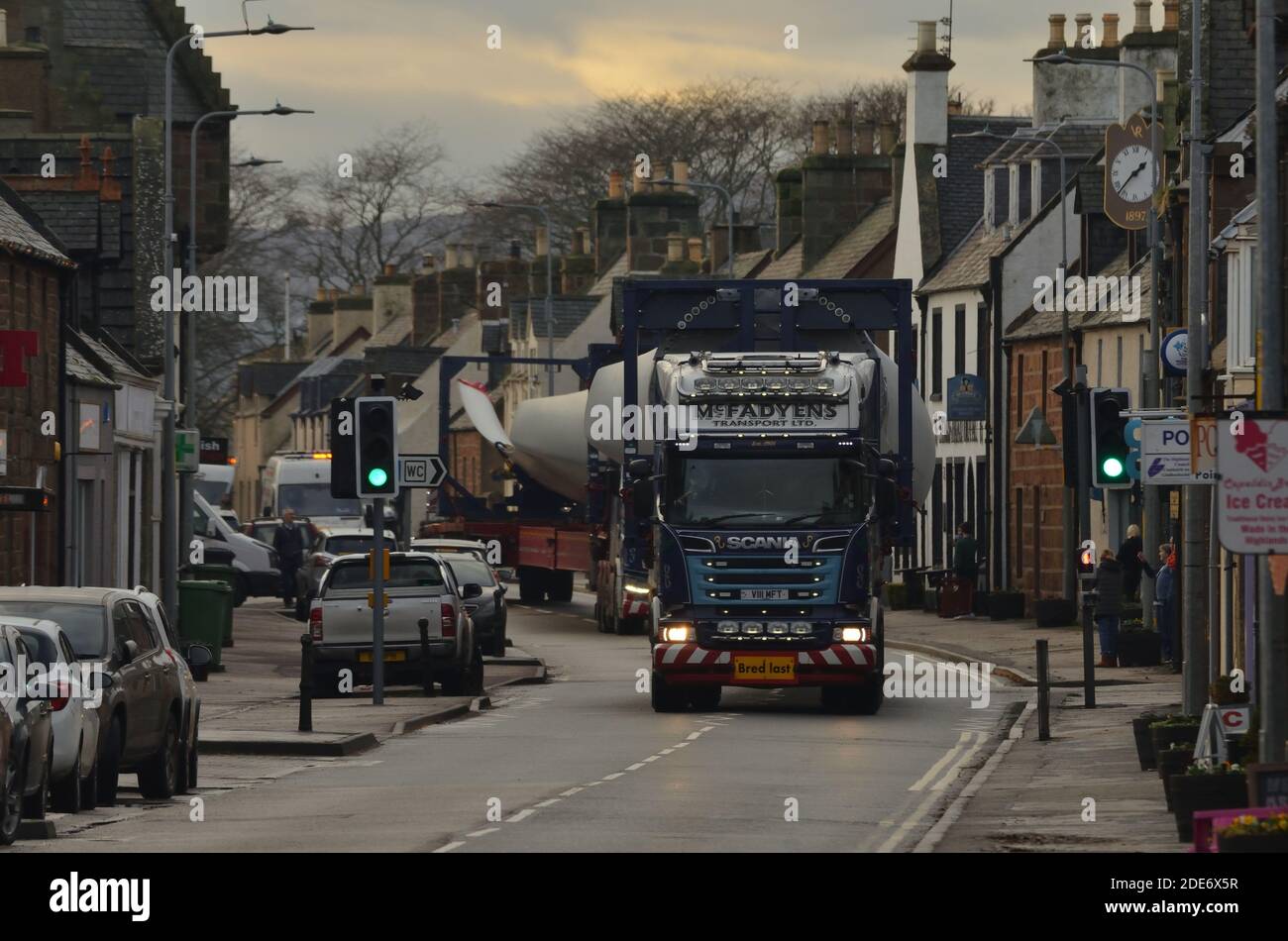 Ein Konvoi von Spezialfahrzeugen entlang der Hauptstraße in Golspie Dorf, Schottische Highlands, mit einer Lieferung von Windturbinenblättern. Stockfoto