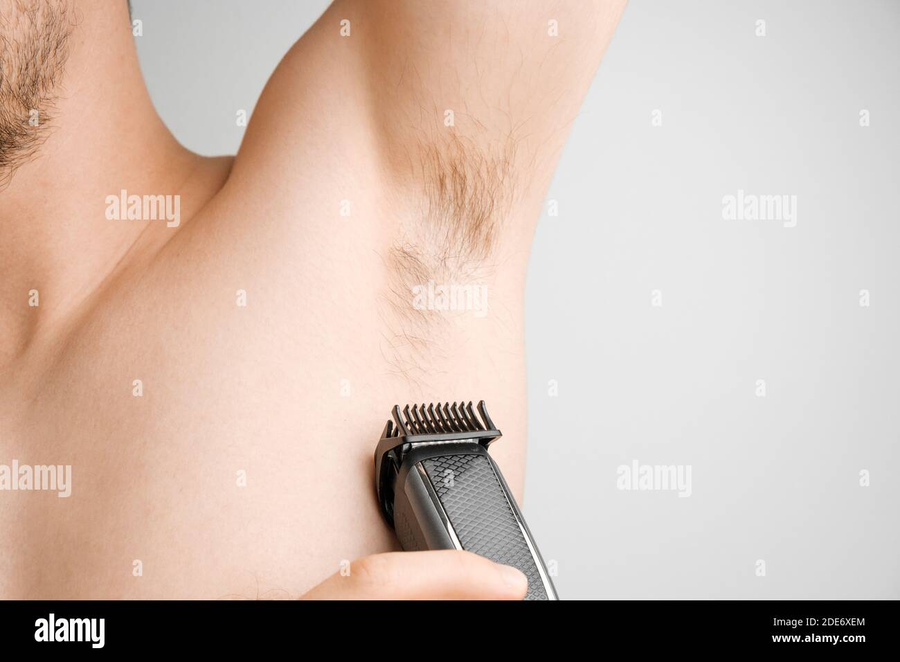 Nahaufnahme Mann rasiert haarige Achselhöhlen mit einem elektrischen Rasiermesser. Unrasierte Achselhöhlen oder Achselhöhlen. Enthaarung und Haarentfernung Verfahren mit Trimmer. Körper Stockfoto