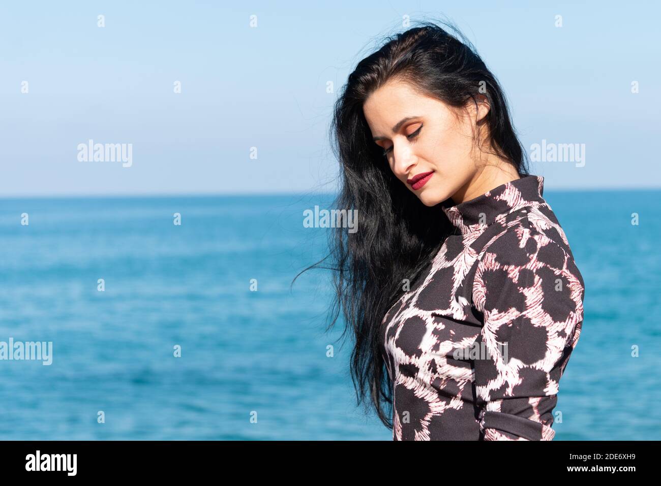 Nahaufnahme Porträt von schönen stilvollen eleganten selbstbewussten jungen Frau mit langen dunklen Haaren und roten Lippenstift, entspannend genießen Sommersonne mit Meer in Stockfoto