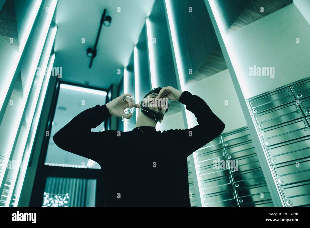 Junge Hipster Mann drinnen unter Lumineszenz Neonlicht versteckt seine Gesicht Stockfoto