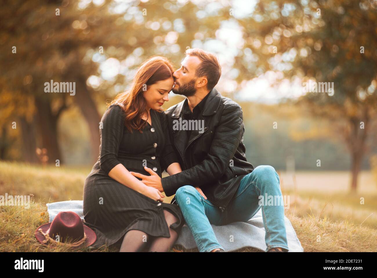 Foto von glücklichen schwangeren Paar auf der Bank im Park sitzen, schöne Stirn Kuss. Stockfoto