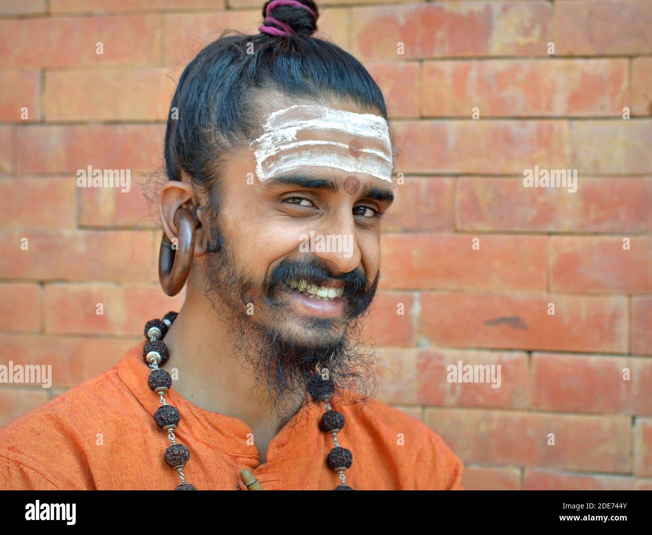 Fröhlicher junger Hindu-Shaivite Gorakhnathi (Kanphata) Yogi-Mönch mit Top-Brötchen und die riesigen Signature-Ohrringe des Gorakh-Nath-Ordens posiert für die Kamera. Stockfoto