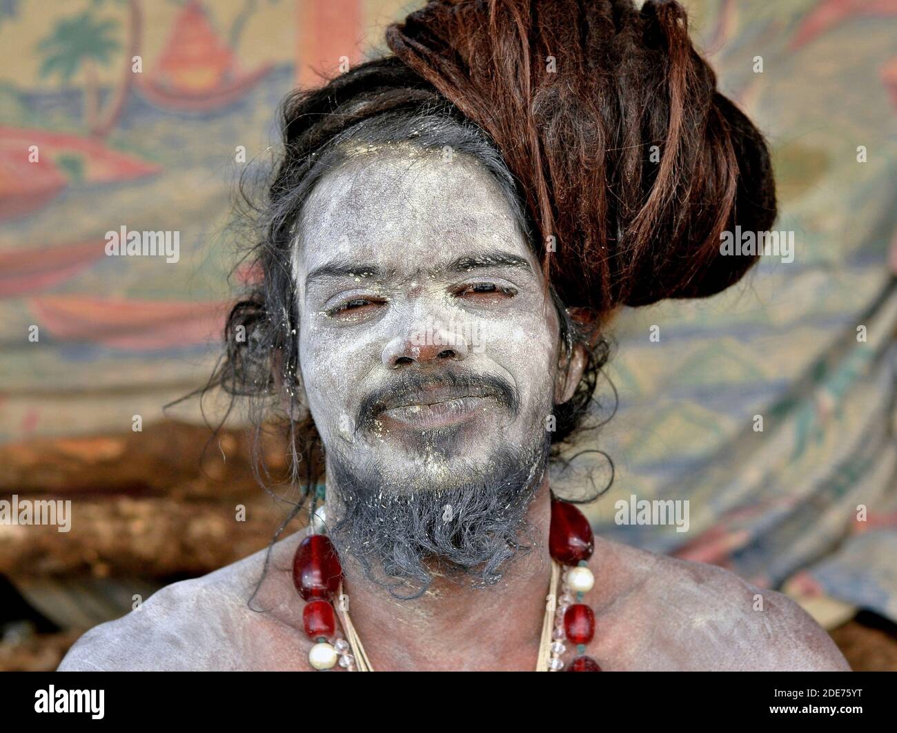Der junge indische Hindu-Shaivite Sadhu und Yogi mit dem Schreck und der heiligen weißen Asche (Vibhuti) auf seinem Gesicht, seinem Bart und seinen Schultern posiert für die Kamera. Stockfoto