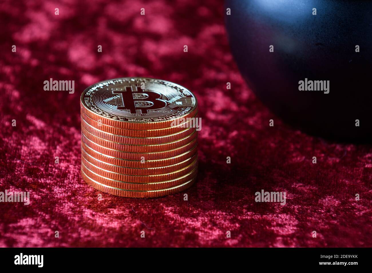 Stapel von Goldbitcoins auf einem roten Samthintergrund, mit schwarzem Topf Stockfoto