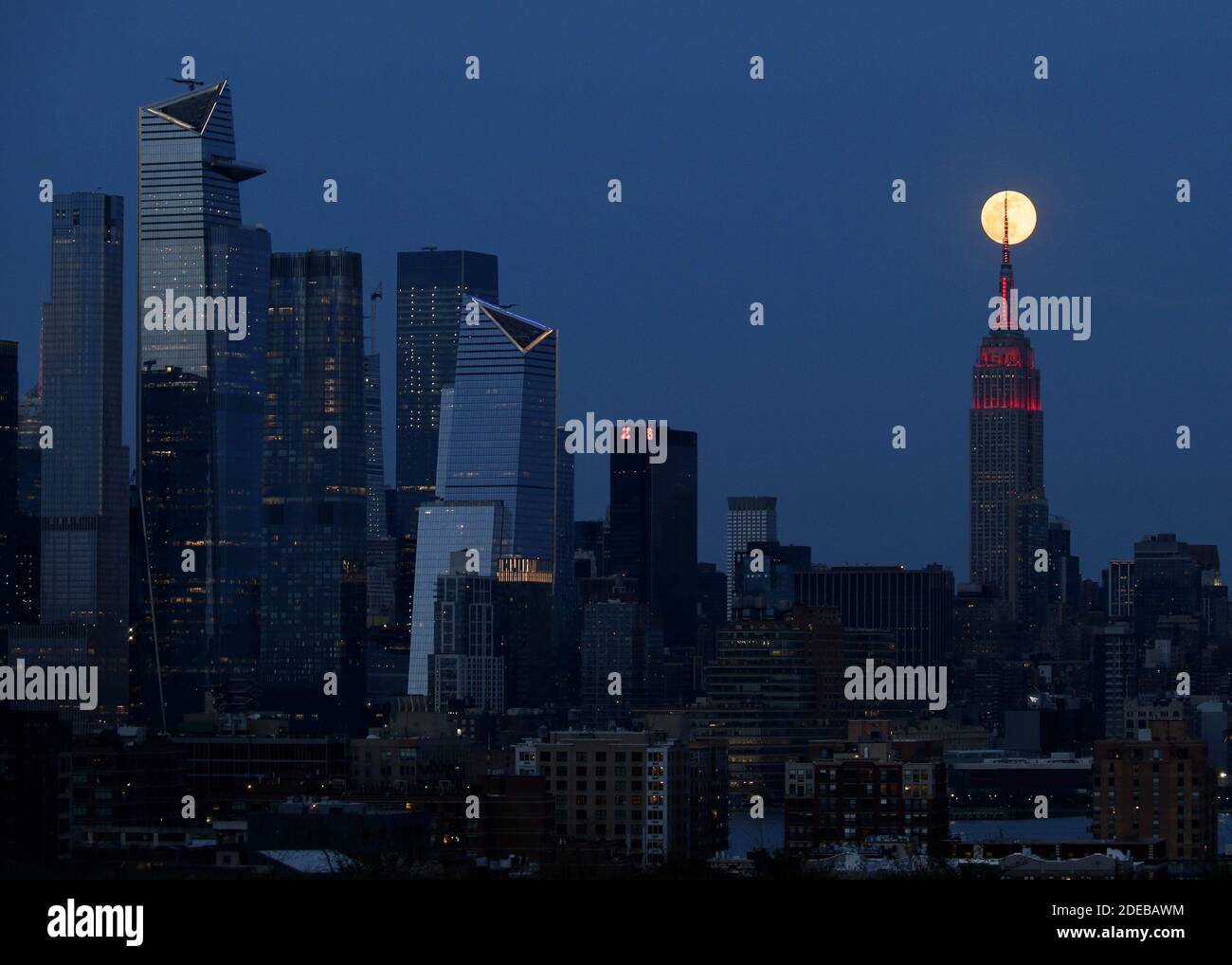 New York, Usa. November 2020. Ein Pink Supermoon erhebt sich hinter dem Empire State Building und der Skyline von Manhattan mit einer roten Lichtanzeige zu Ehren der Rettungskräfte, die am Dienstag, den 7. April 2020 gegen das Coronavirus kämpfen. Während der gesamten COVID-19-Schlacht wurden die charakteristischen weißen Lichter auf dem ESB durch den Herzschlag Amerikas ersetzt, zusammen mit einer weißen und roten Sirene im Mast für heldenhafte Rettungskräfte an der Front des Kampfes." Foto von John Angelillo/UPI Kredit: UPI/Alamy Live Nachrichten Stockfoto