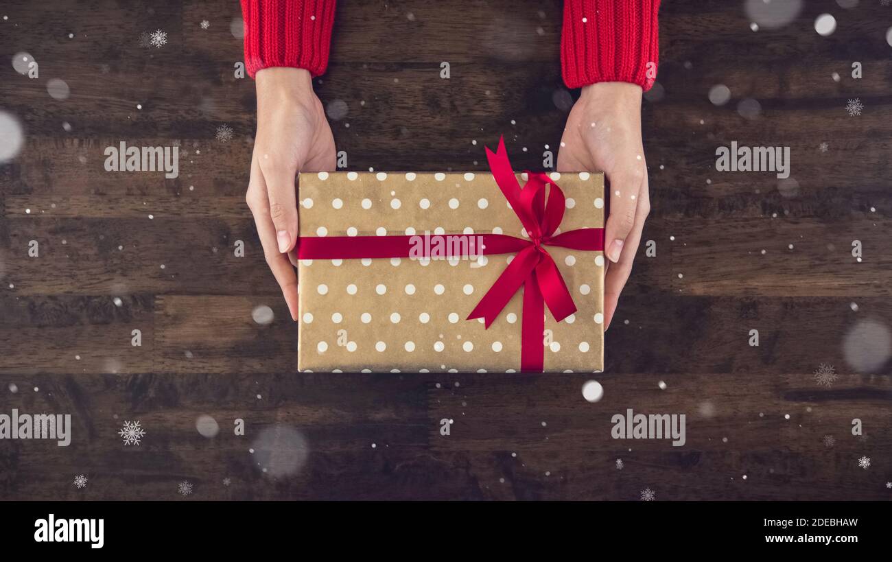 Frau Hände geben christsmas Geschenkbox mit gepunkteten Muster verpackt Papier und rotes Band Draufsicht auf Holz Tisch Hintergrund Mit Schnee Stockfoto