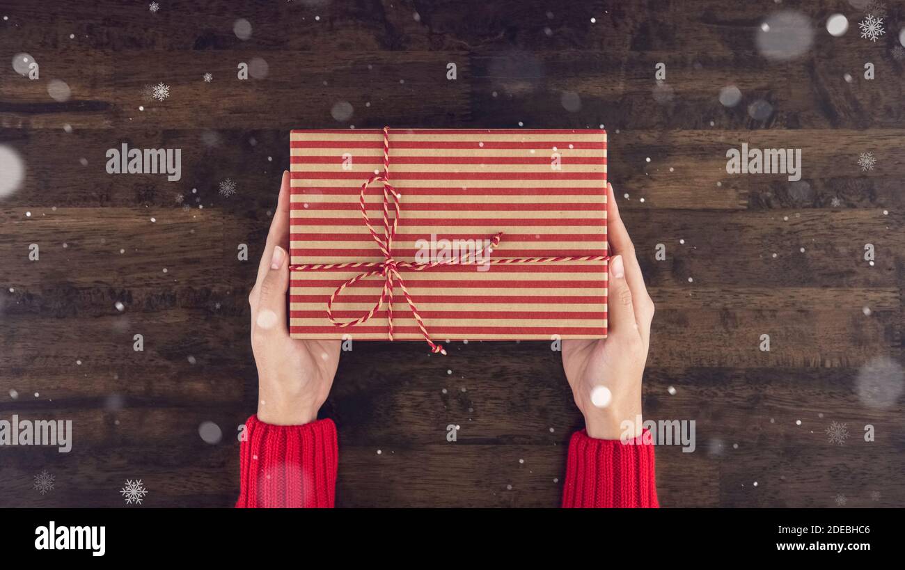 Frau Hände geben christsmas Geschenkbox Draufsicht auf Holz Tischhintergrund mit Schneefall Stockfoto
