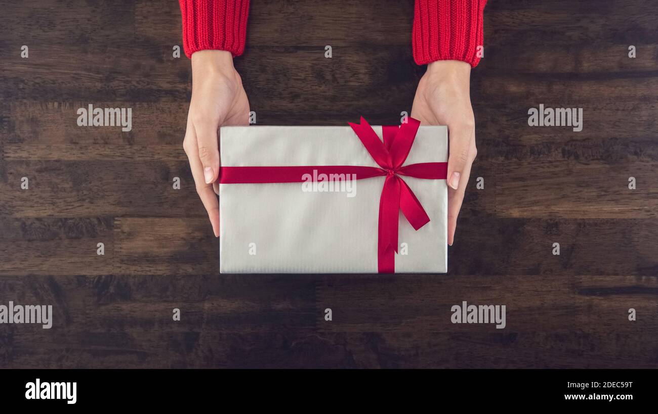 Frau Hände geben christsmas Geschenkbox mit grauem Papier verpackt Draufsicht auf Holztisch Hintergrund Stockfoto