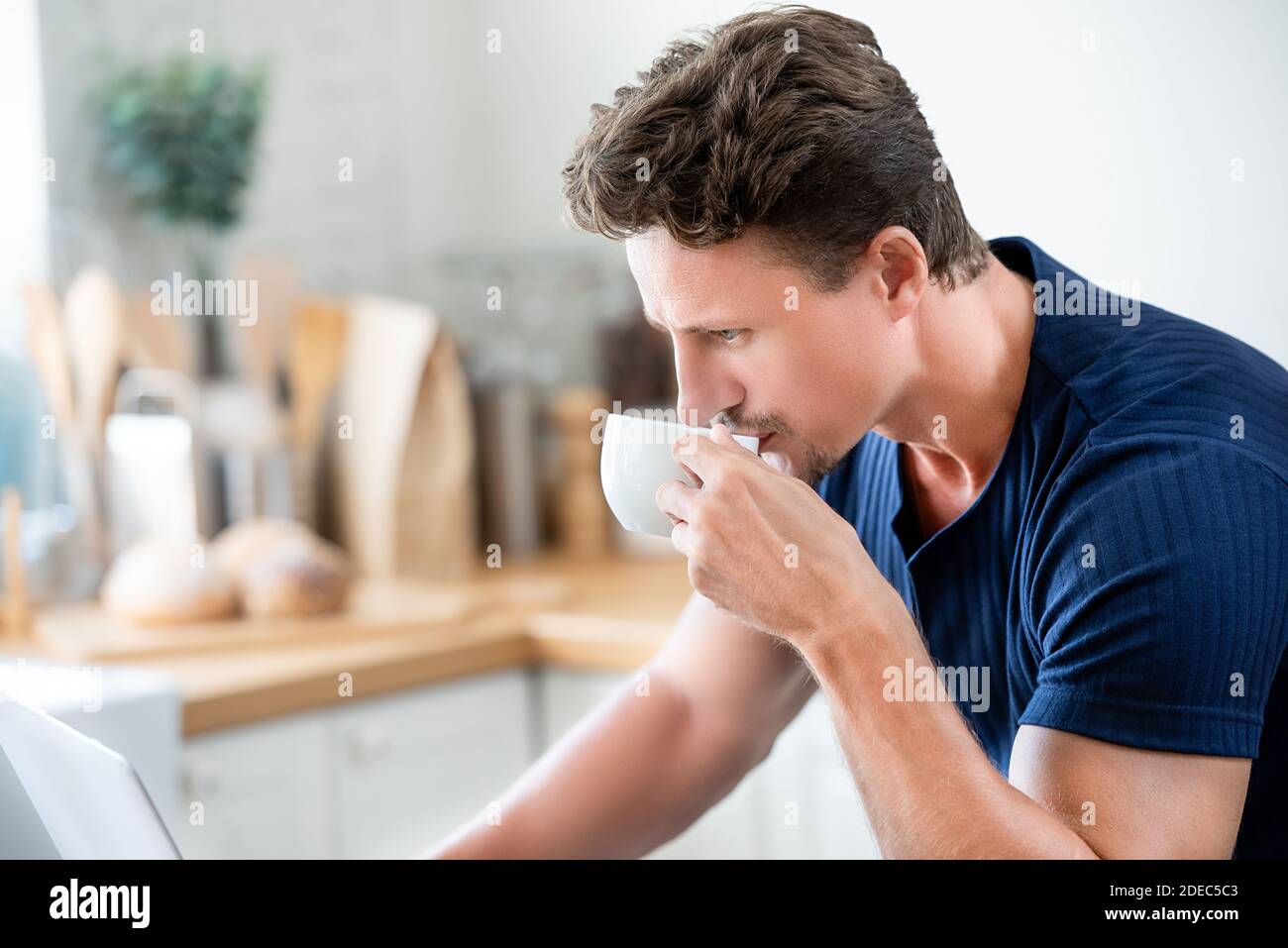 Zwangloser Mann, der morgens Kaffee trinkt, während er ernsthaft arbeitet Auf Laptop-Computer zu Hause Stockfoto