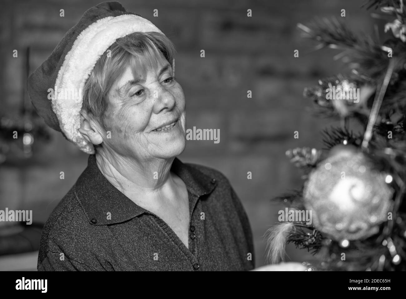 Glückliche ältere Rentnerin trägt Santa Red hat Dekoration Weihnachtsbaum zu Hause. Stockfoto