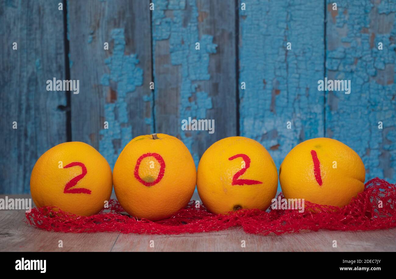 Orangen mit den Zahlen 2021 auf einem hölzernen Hintergrund. Früchte für Weihnachten und Neujahr im Raster. Reife Zitrusfrüchte für das neue Jahr. Stockfoto