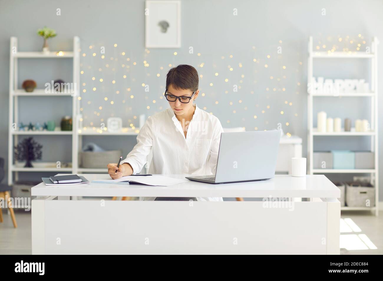 Ernsthafte junge Frau, die sich auf Arbeit oder Studium sitzend konzentriert Schreibtisch mit Laptop zu Hause Stockfoto