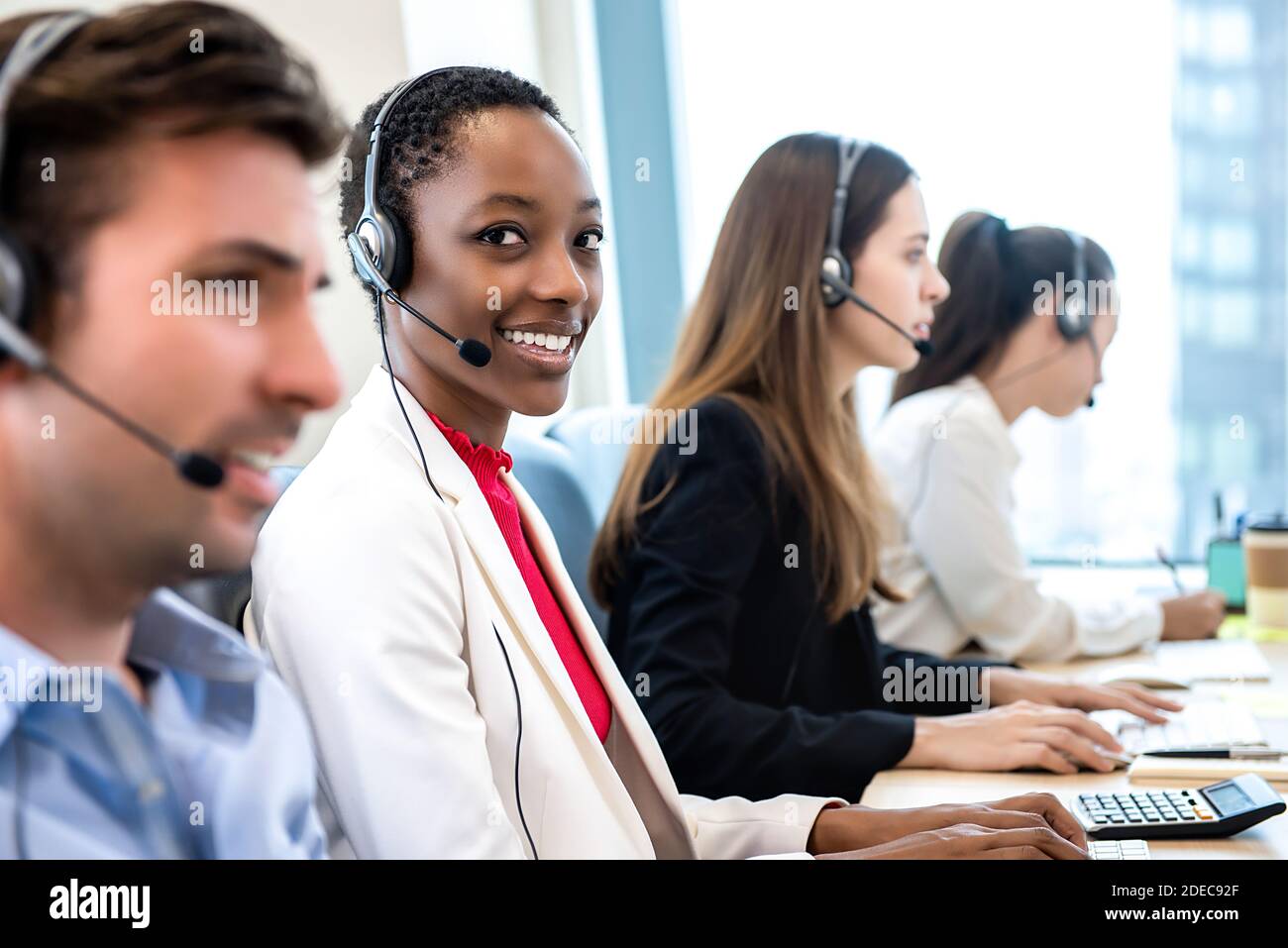 Lächelnd schöne afroamerikanische Frau, die im Callcenter-Büro arbeitet Mit einem vielfältigen Team als Kundendienstmitarbeiter Stockfoto